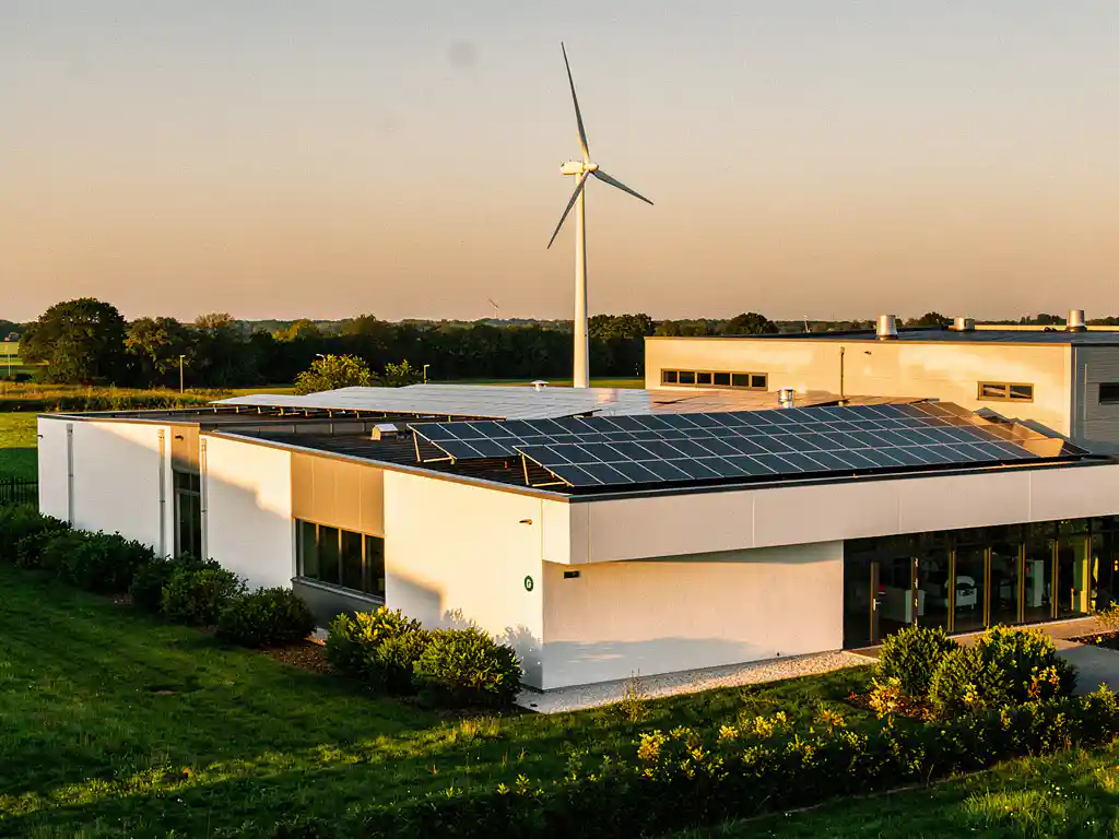 Windturbine en zonnepanelen op een modern Nederlands industriegebouw tijdens het gouden uur, omgeven door weelderig groen.